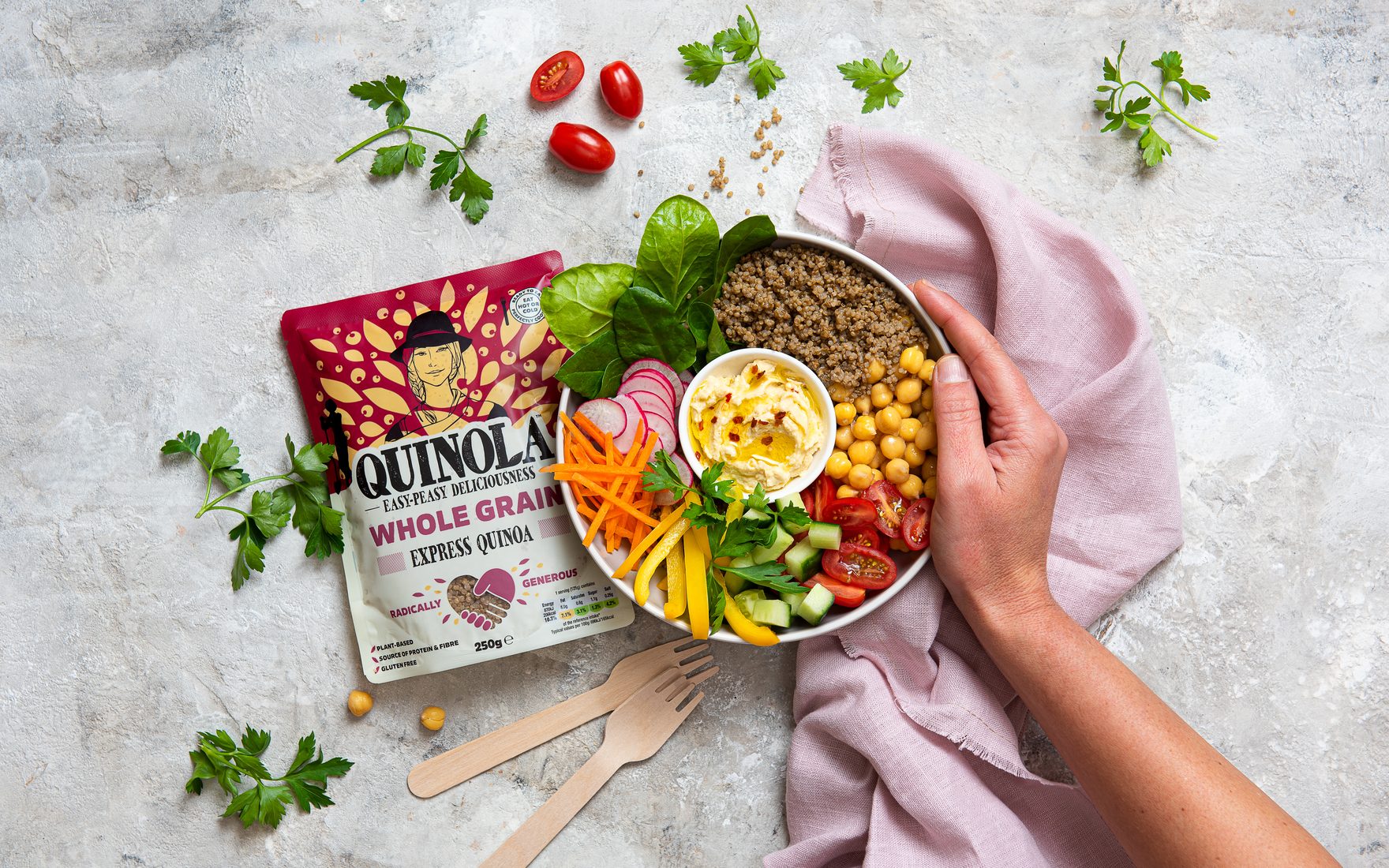 A Quinola Express pouch beside a bowl of quinoa, salad and hummus