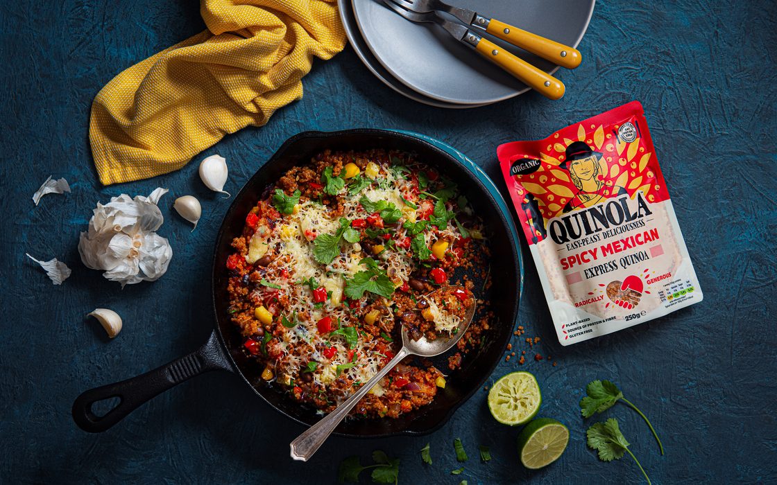 A Quinola Express pouch beside a skillet of cooked quinoa