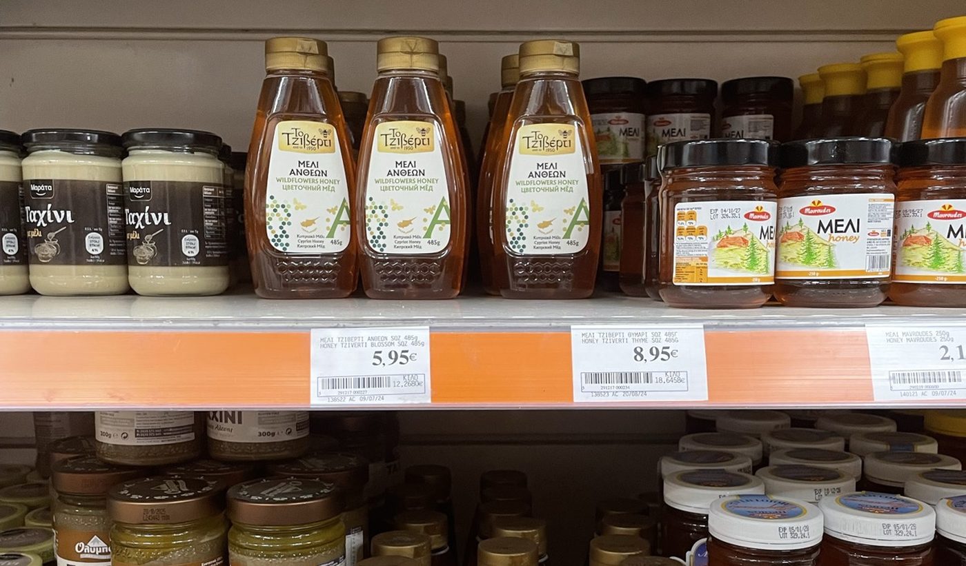 A supermarket honey shelf, Tziverti squeeze bottles beside competitor jars printed with mountain and forest scenes